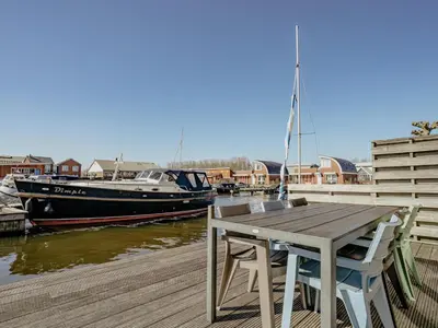 a wooden table and chairs on a dock with a boat at Westergeest in Uitgeest