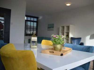 a white table with yellow chairs and a vase of flowers at Holiday apartment Seapaerdje in Bergen aan Zee
