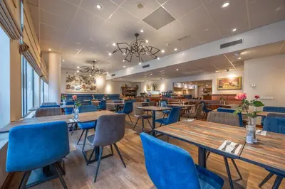 a restaurant with wooden tables and blue chairs at Amrâth Grand Hotel Frans Hals in Haarlem