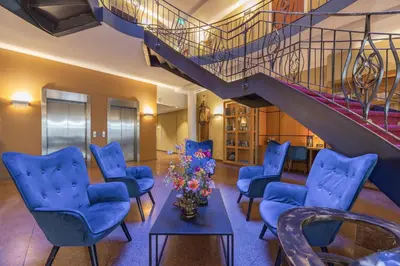 a living room with blue chairs and a staircase at Amrâth Grand Hotel Frans Hals in Haarlem