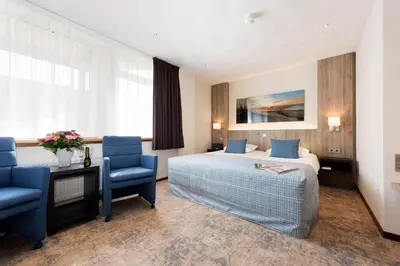 a hotel room with a bed and two blue chairs at Strandhotel de Vassy in Egmond aan Zee