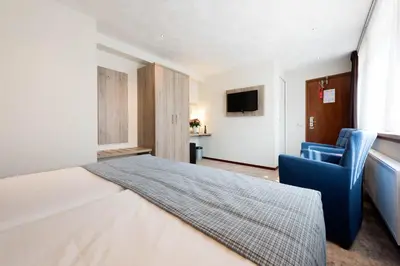 a hotel room with a bed and a blue chair at Strandhotel de Vassy in Egmond aan Zee