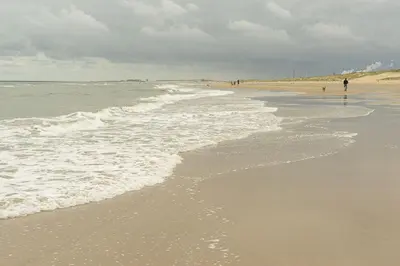 a beach with people walking on the sand and waves at Hotel De Weyman in Santpoort-Noord