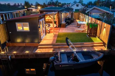 a small house on a dock with a boat on the water at Cabana incl boat, jacuzzi,subboarts on a quiet park with private parking in Loosdrecht