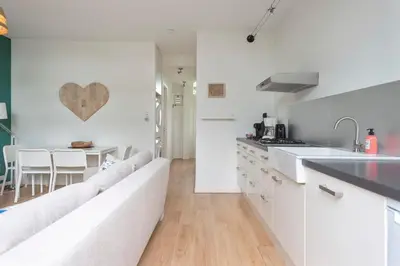 a white kitchen with a long couch and a table at 't Schelpje with free parking in Zandvoort