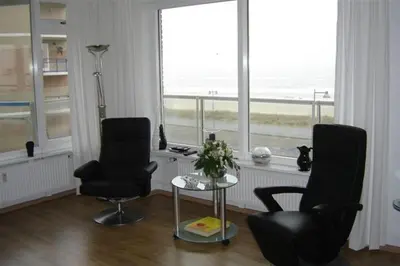 a living room with two chairs and a table and windows at Sterflat 87 in Egmond aan Zee