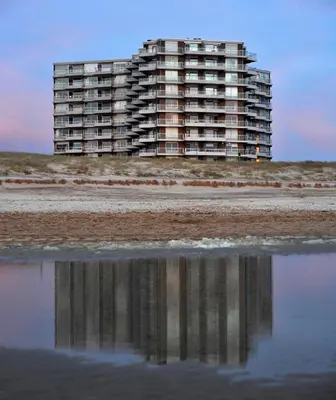 a building on the beach with a reflection in the water at Sterflat 97 in Egmond aan Zee