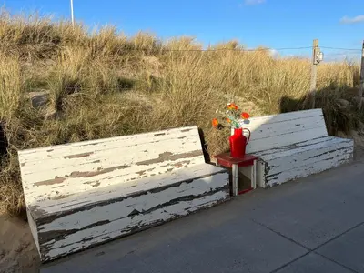 two wooden benches with flowers on a side table at Sterflat 97 in Egmond aan Zee