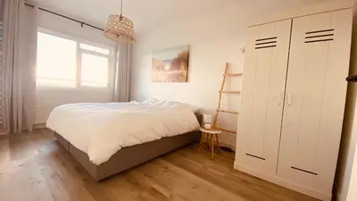 a white bedroom with a bed and a window at Sterflat 119 in Egmond aan Zee
