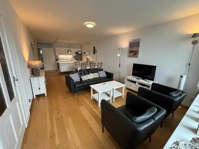 a living room with black leather furniture and a tv at Sterflat 129 in Egmond aan Zee