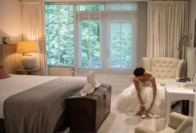a woman in a white wedding dress sitting on a bed at Buitenplaats de Bergse Bossen in Driebergen