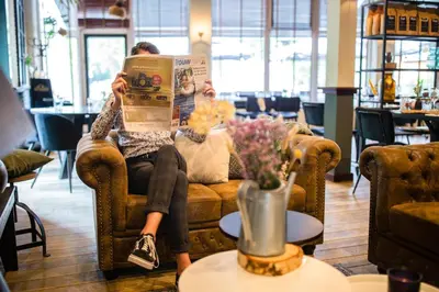 a person sitting on a couch reading a newspaper at Buitenplaats de Bergse Bossen in Driebergen