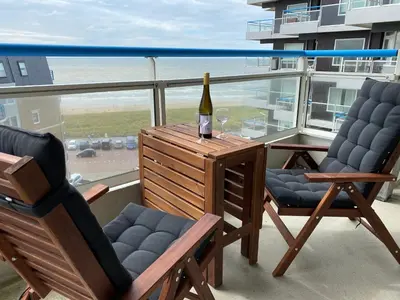 a bottle of wine and two chairs on a balcony at Sterflat 173 in Egmond aan Zee