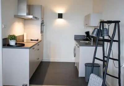 a small kitchen with white cabinets and a ladder at Sterflat 179 in Egmond aan Zee