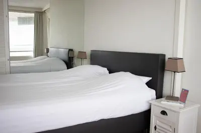 a bedroom with two beds with white sheets and a window at Sterflat 179 in Egmond aan Zee