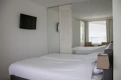 a bedroom with two beds and a tv on the wall at Sterflat 179 in Egmond aan Zee