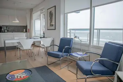a living room with chairs and a table and a kitchen at Sterflat 185 in Egmond aan Zee