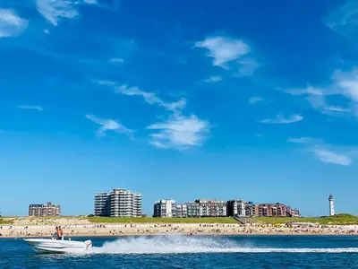 a boat in the water with a beach and buildings at Sterflat 189 in Egmond aan Zee