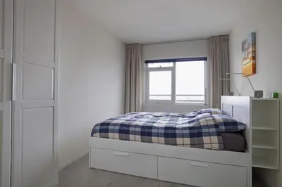 a white bedroom with a bed and a window at Sterflat 199 in Egmond aan Zee