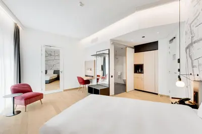 a bedroom with a white bed and a living room at IntercityHotel Leiden in Leiden