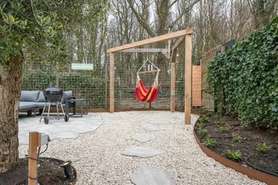 a patio with a hammock and a bench and a grill at Kahakai Beach House - Unique Outdoor Kitchen - next to local lake and 15 min. the from beach in Noordwijkerhout