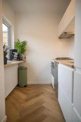 a kitchen with white cabinets and a wooden floor at Kahakai Beach House - Unique Outdoor Kitchen - next to local lake and 15 min. the from beach in Noordwijkerhout