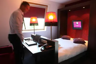 a man standing in a bedroom with a bed and a desk at Hotel Mijdrecht Marickenland in Mijdrecht