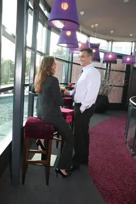 a man and a woman sitting at a bar with purple lamps at Hotel Mijdrecht Marickenland in Mijdrecht
