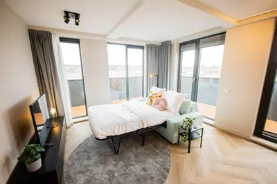 a room with a bed and a couch and windows at Alphabet Apartments - Kerkstraat 71 in Hilversum