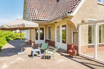 a house with a patio with chairs and an umbrella at Villa Duin en Strand in Bergen aan Zee