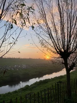a sunset over a river with a fence at Rosa's zonnige huisje bij duinen bos en strand in Warmenhuizen