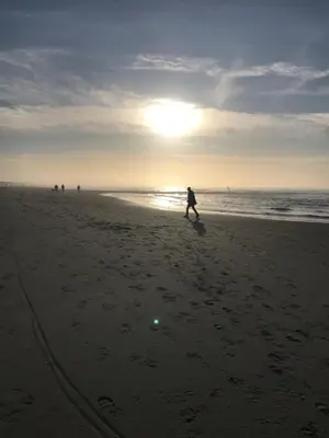 a person walking on the beach with the sun in the background at Rosa's zonnige huisje bij duinen bos en strand in Warmenhuizen