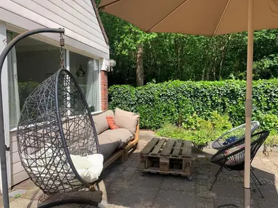 a patio with a swing and a couch and an umbrella at Holiday Home near Noordwijk Beach in Noordwijkerhout