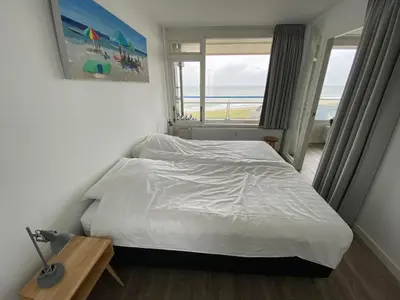 a bedroom with a white bed and a window at Sterflat 219 in Egmond aan Zee