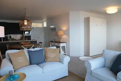 a living room with two white couches and a kitchen at Sterflat 241 in Egmond aan Zee