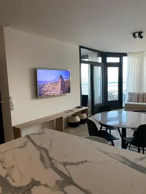 a living room with a table and a tv on the wall at Sterflat 261 in Egmond aan Zee