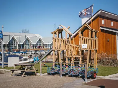 a wooden playground with a slide in front of a marina at Modern Waterfront Retreat in Uitgeest