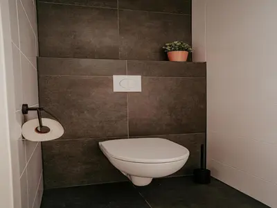 a bathroom with a toilet in a brown tiled wall at Modern Waterfront Retreat in Uitgeest