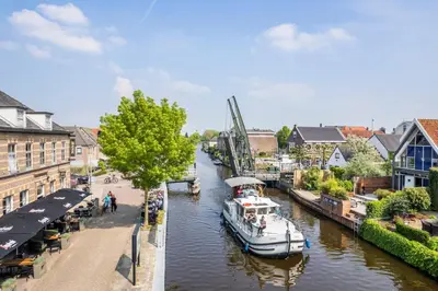 a boat is docked on a river in a city at Hotel Over de Brug in Haastrecht