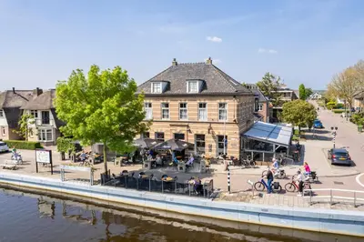 a building next to a river with people sitting at tables at Hotel Over de Brug in Haastrecht