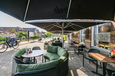 an outdoor patio with tables and chairs and an umbrella at Hotel Over de Brug in Haastrecht