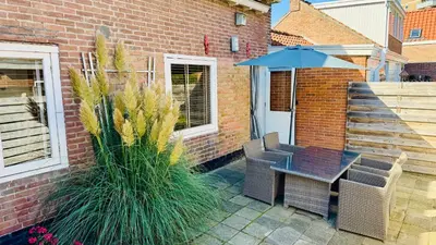 a patio with a table and chairs and an umbrella at Vakantiehuis Voor Anker in Egmond aan Zee