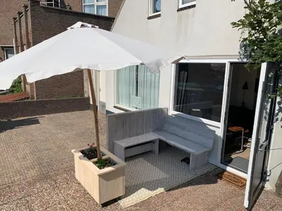 a bench with an umbrella on a patio at Hello Noordwijk - Familiehuis Quarles van Uffordstraat 77 in Noordwijk aan Zee