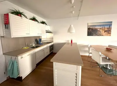 a kitchen with white cabinets and a dining table at Sterflat 101 in Egmond aan Zee