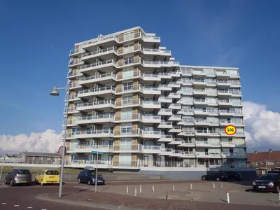 a tall building with cars parked in a parking lot at Sterflat 101 in Egmond aan Zee