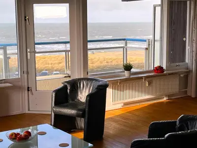 a living room with a chair and a table and windows at Sterflat 101 in Egmond aan Zee