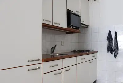 a kitchen with white cabinets and a sink and a tv at Zeezand in Egmond aan Zee