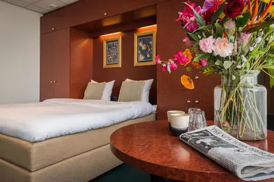 a hotel room with two beds and a table with flowers at Prominent Inn Hotel in Noordwijk aan Zee