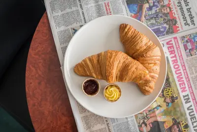 a plate with croissants and mustard on a newspaper at Prominent Inn Hotel in Noordwijk aan Zee