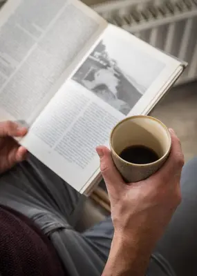 a person reading a book and a cup of coffee at Prominent Inn Hotel in Noordwijk aan Zee